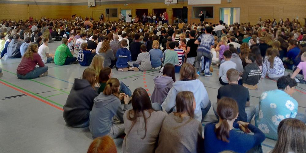 Schülerinnen und Schüler sitzen in der Turnhalle und feiern gemeinsam einen Gottesdienst.