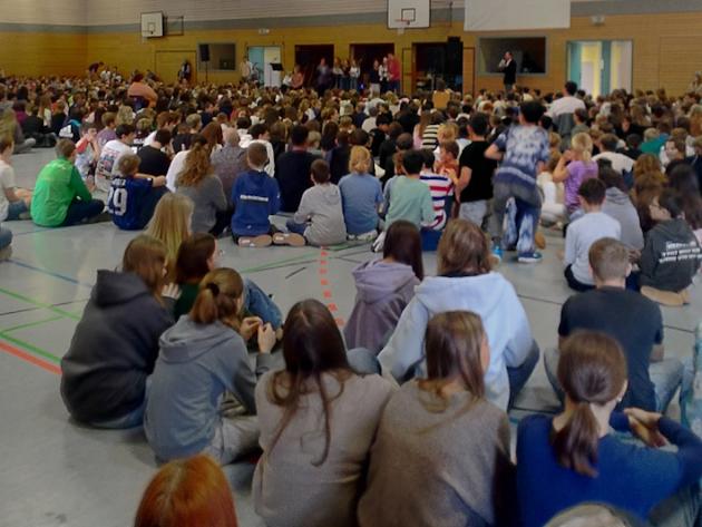 Schülerinnen und Schüler sitzen in der Turnhalle und feiern gemeinsam einen Gottesdienst.