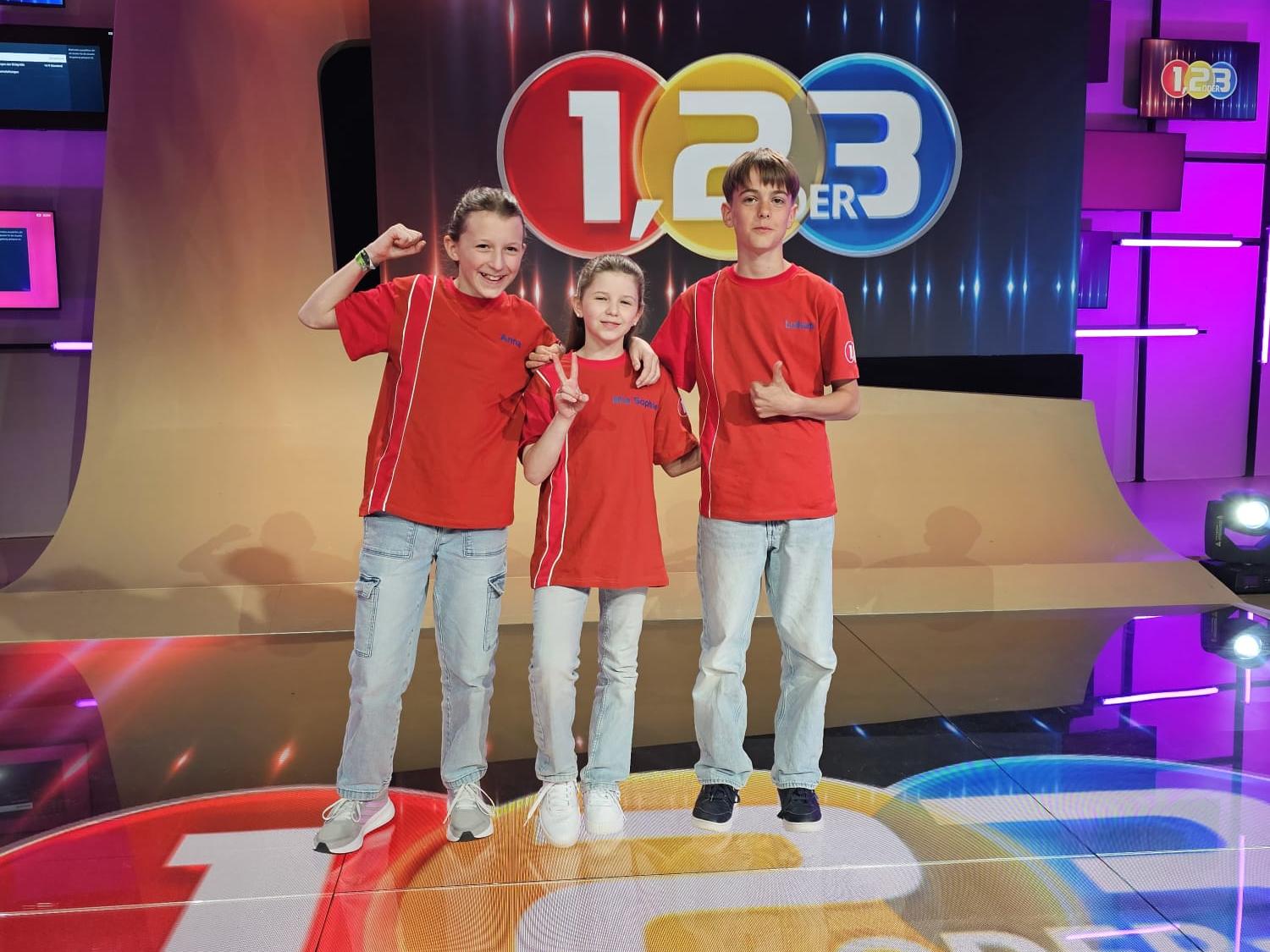Drei Kinder stehen vor dem 123-Logo.