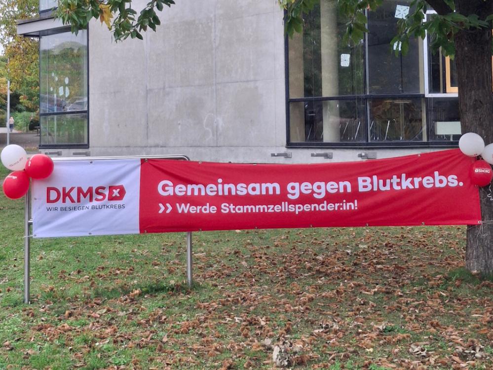 Ein rotes Banner mit der Aufschrift 'Gemeinsam gegen Blutkrebs' ist vor der Schule aufgespannt.
