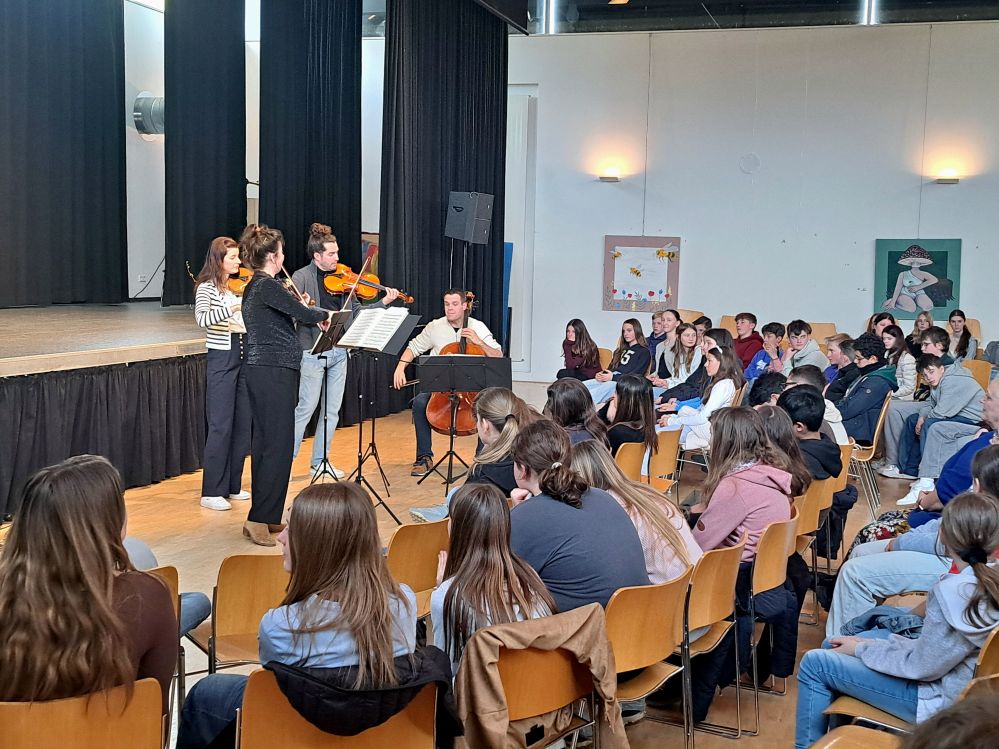 Schüler sitzen in der Aula und hören dem Aris-Quartett zu, das vor der Bühne musiziert.