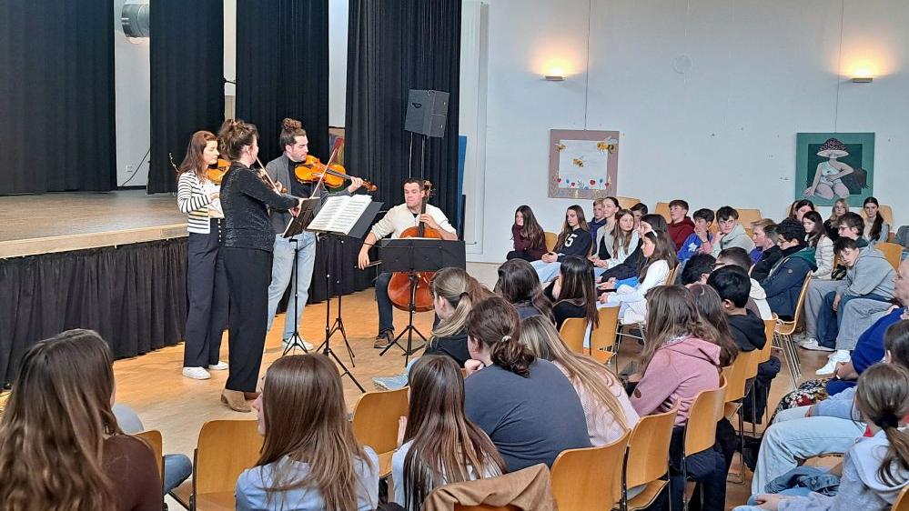 Schüler sitzen in der Aula und hören dem Aris-Quartett zu, das vor der Bühne musiziert.