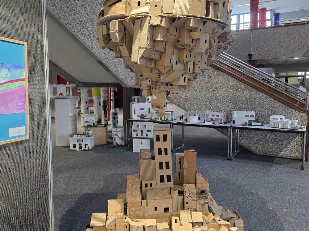 Zwei Städte aus Karton wachsen von Boden und Himmel einander entgegen.