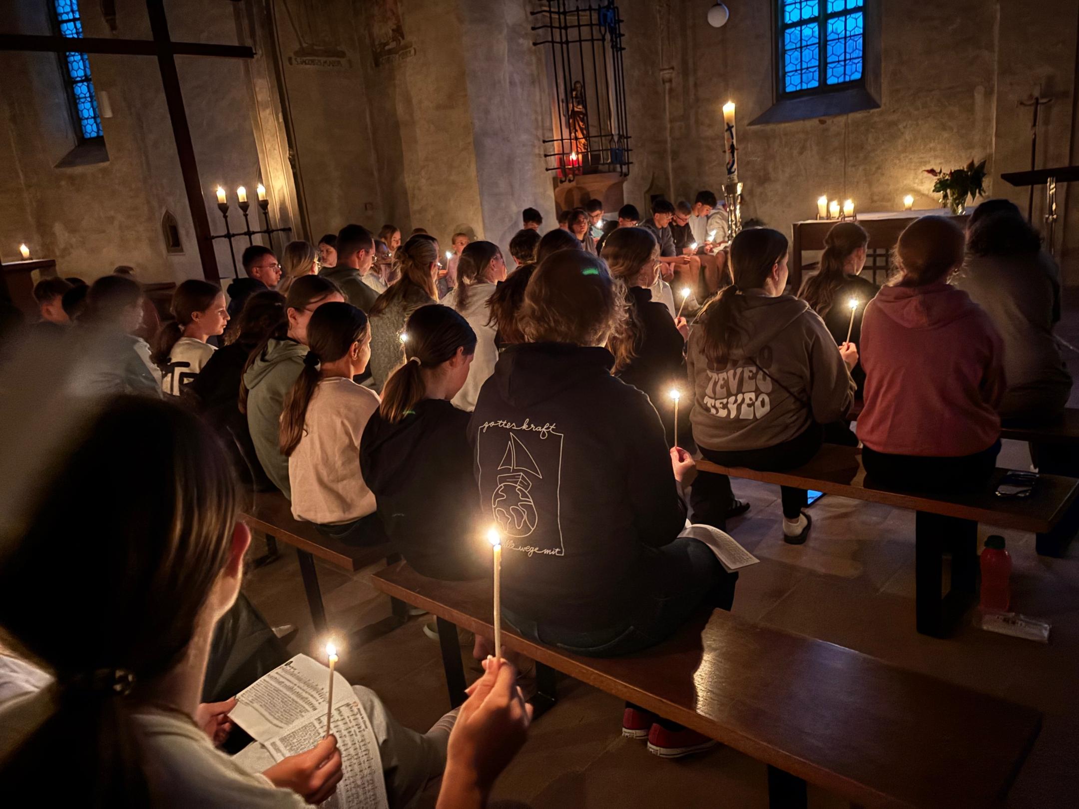 Jugendliche verschiedenen Alters feiern mit Kerzen einen Gottesdienst.