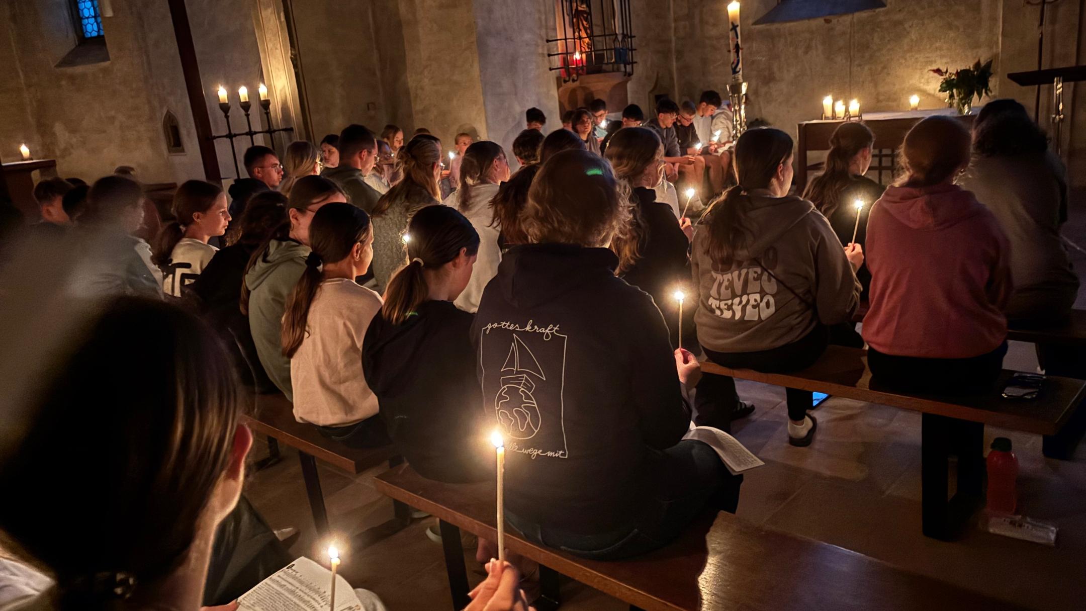 Jugendliche verschiedenen Alters feiern mit Kerzen einen Gottesdienst.