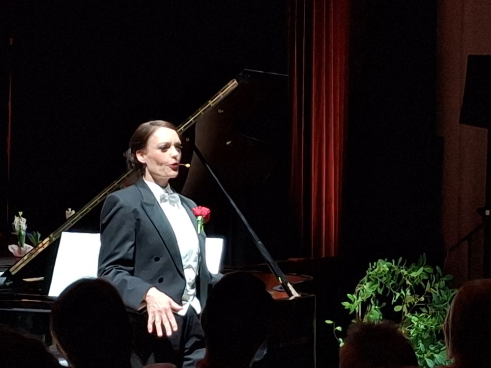 Die Künstlerin steht im Frack vor dem Flügel.