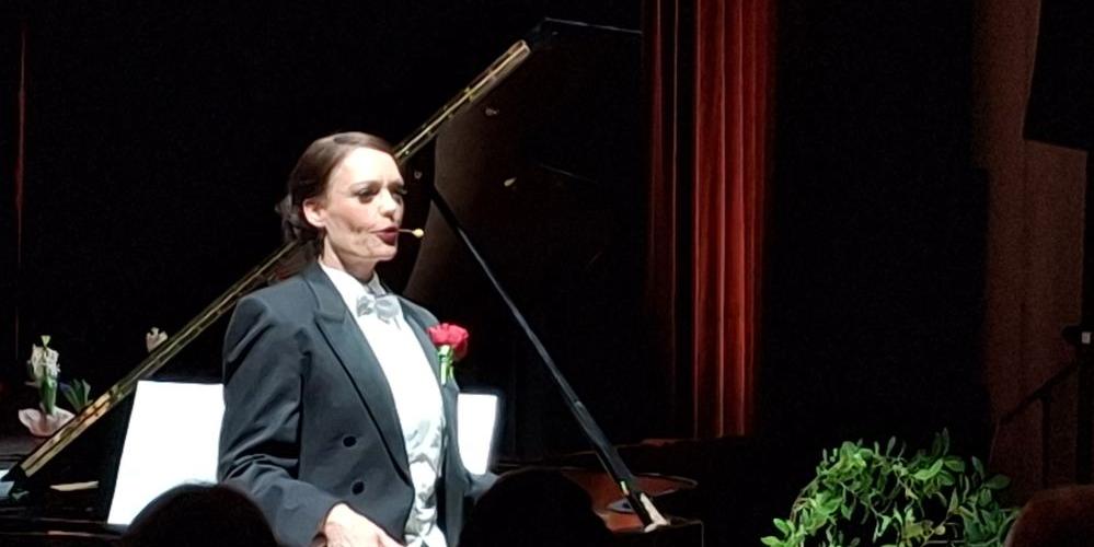 Die Künstlerin steht im Frack vor dem Flügel.