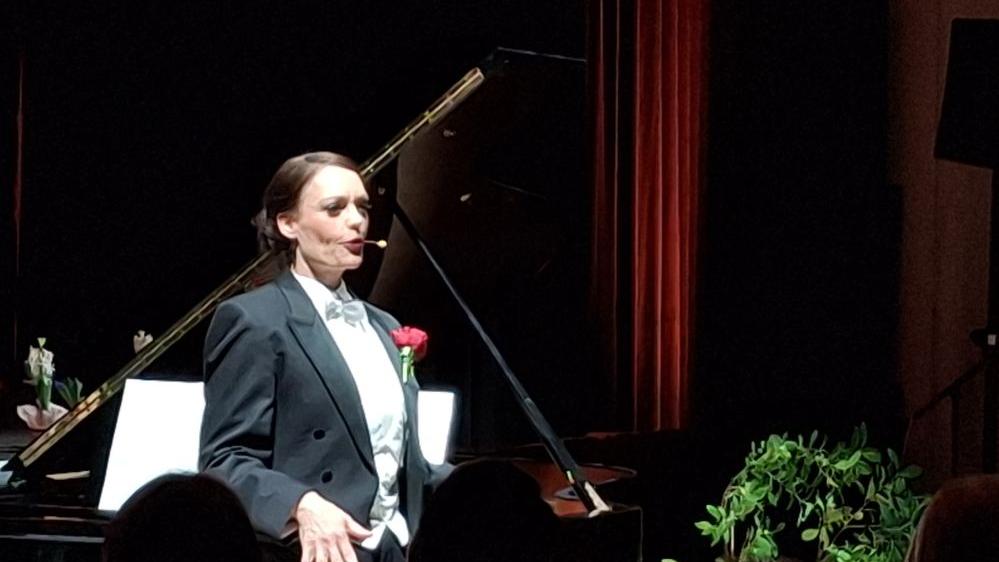 Die Künstlerin steht im Frack vor dem Flügel.