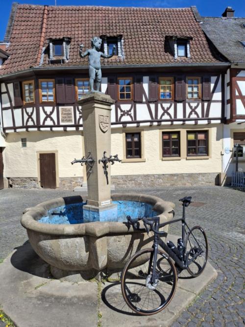 Ein Rad lehnt an einem Brunnen vor einem Fachwerkhaus.