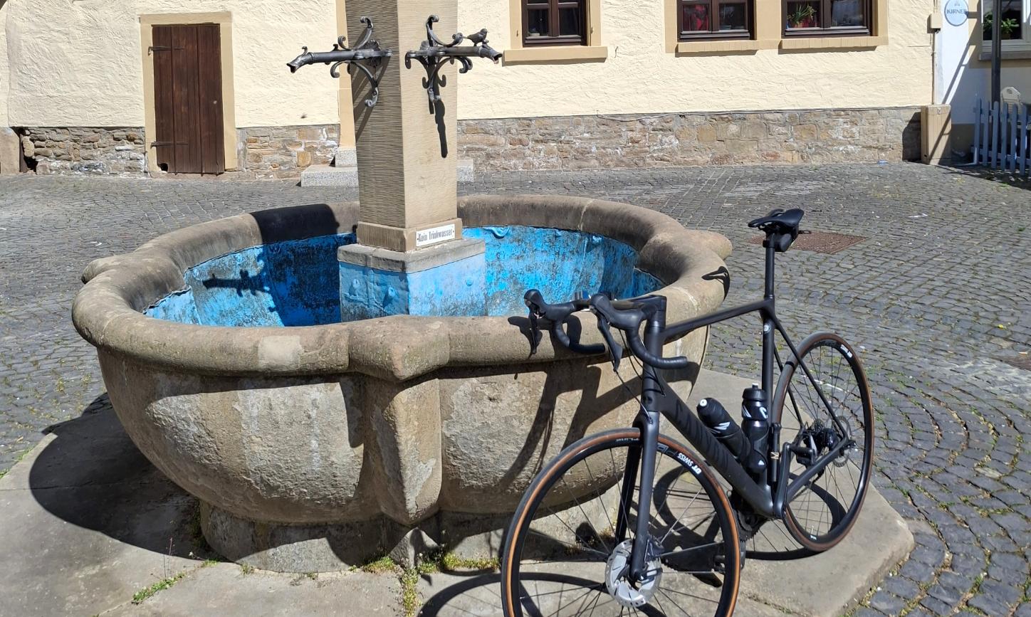 Ein Fahrrad lehnt an einem Brunnen vor einem Fachwerkhaus.