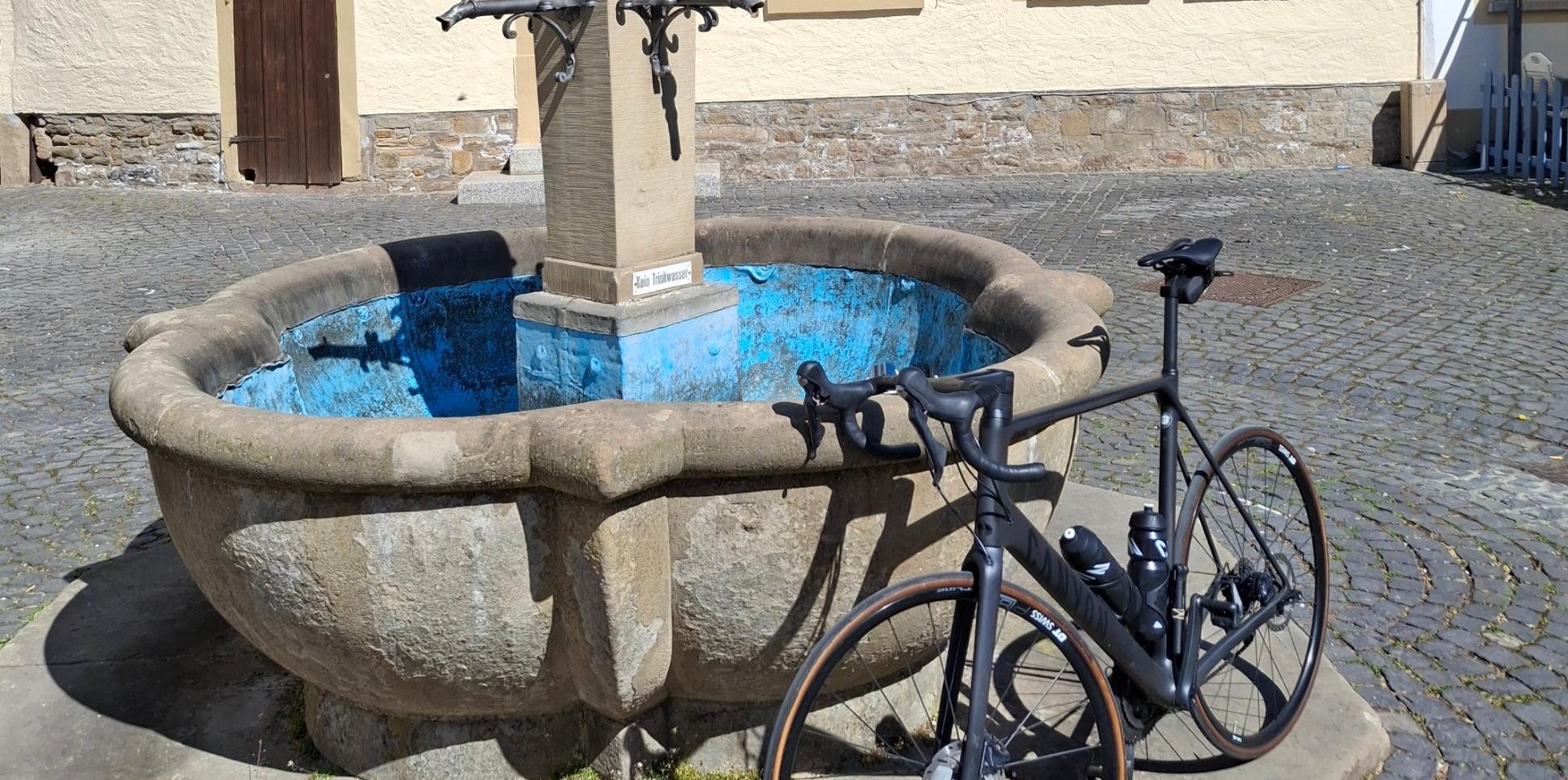 Ein Fahrrad lehnt an einem Brunnen vor einem Fachwerkhaus.