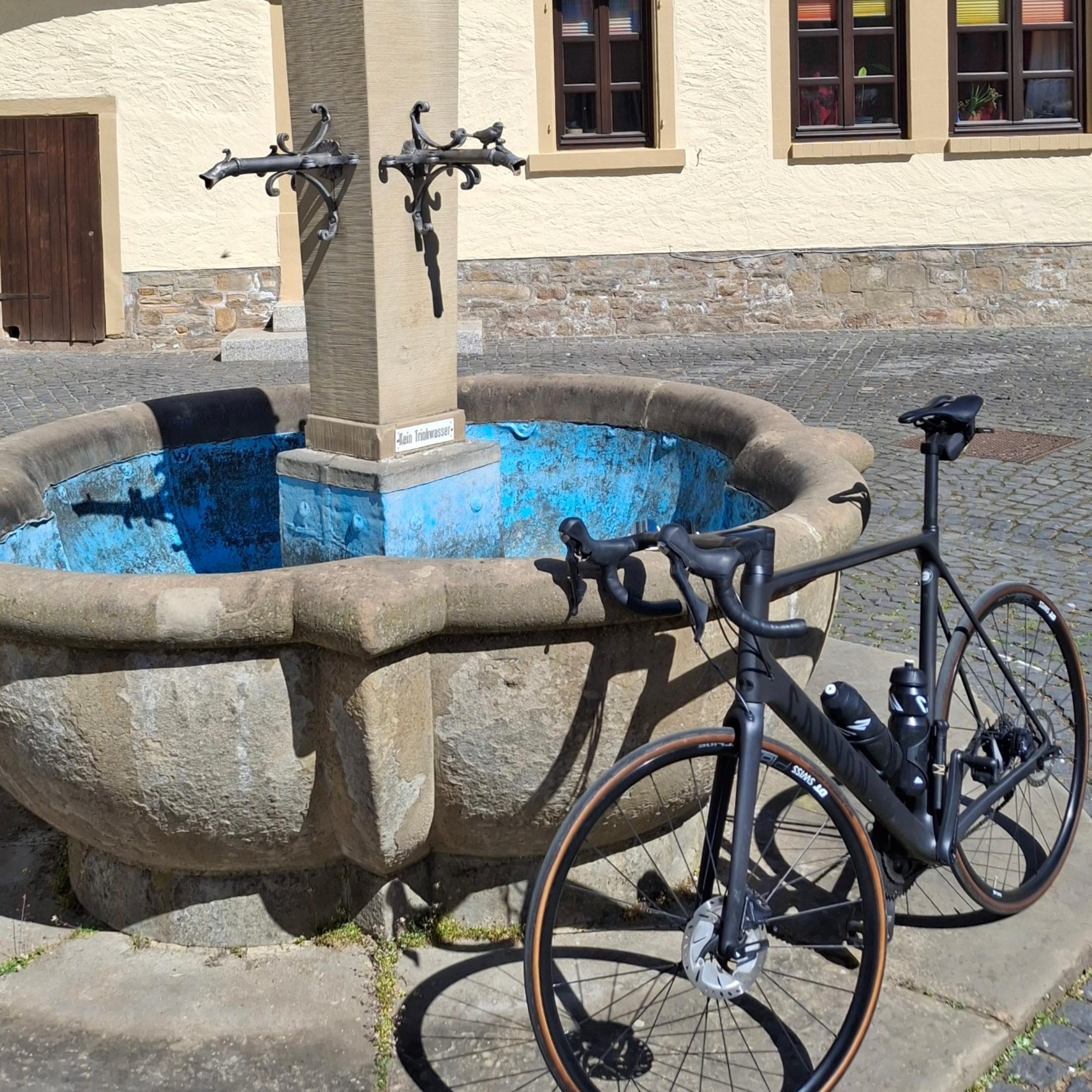 Ein Fahrrad lehnt an einem Brunnen vor einem Fachwerkhaus.