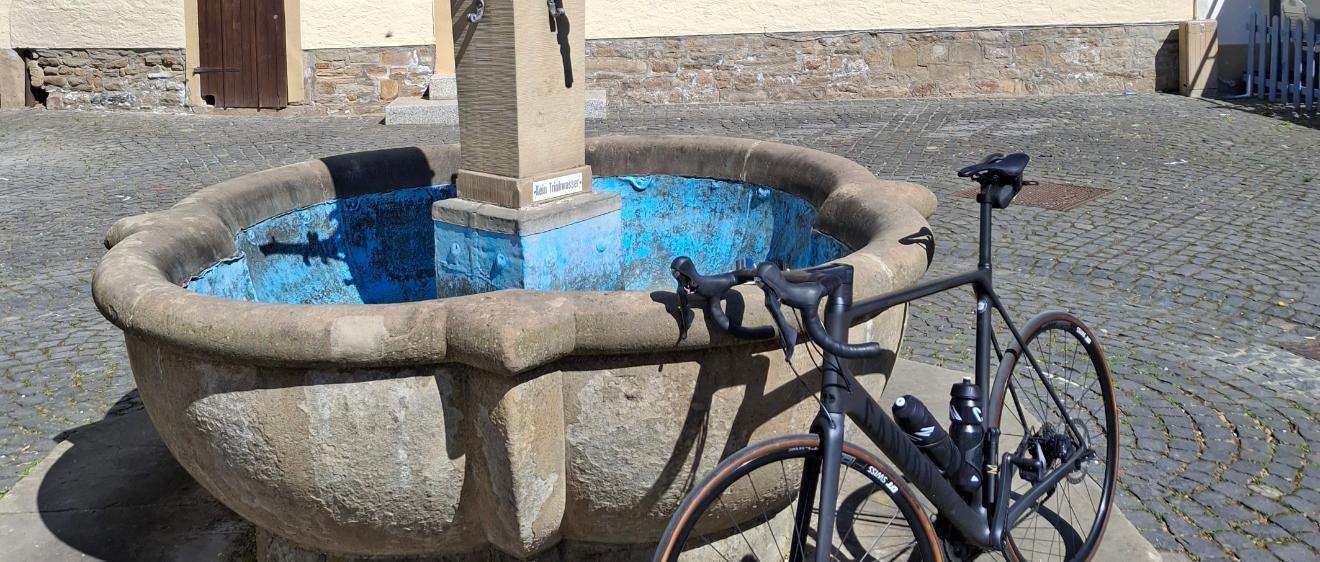 Ein Fahrrad lehnt an einem Brunnen vor einem Fachwerkhaus.