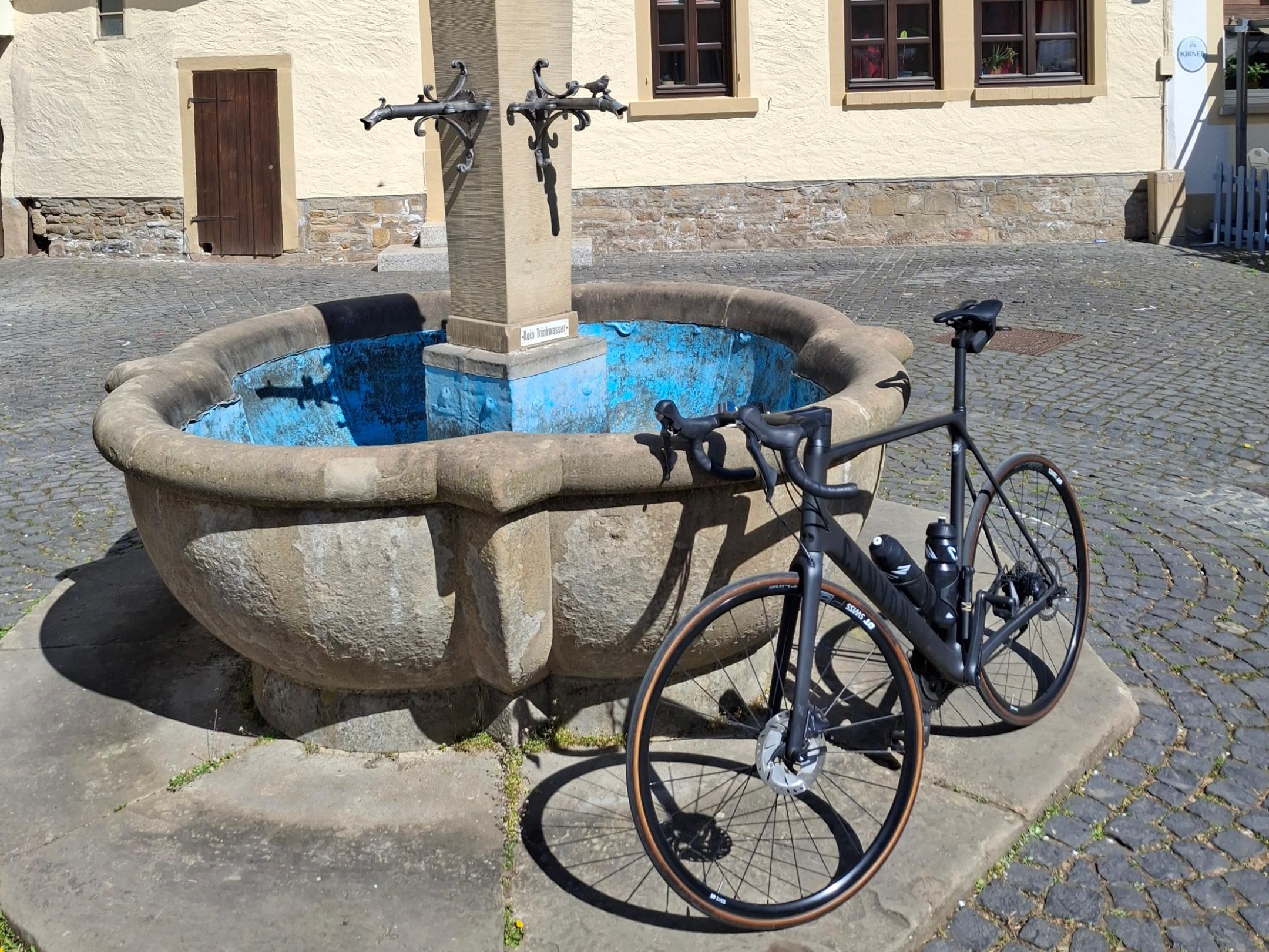 Ein Fahrrad lehnt an einem Brunnen vor einem Fachwerkhaus.
