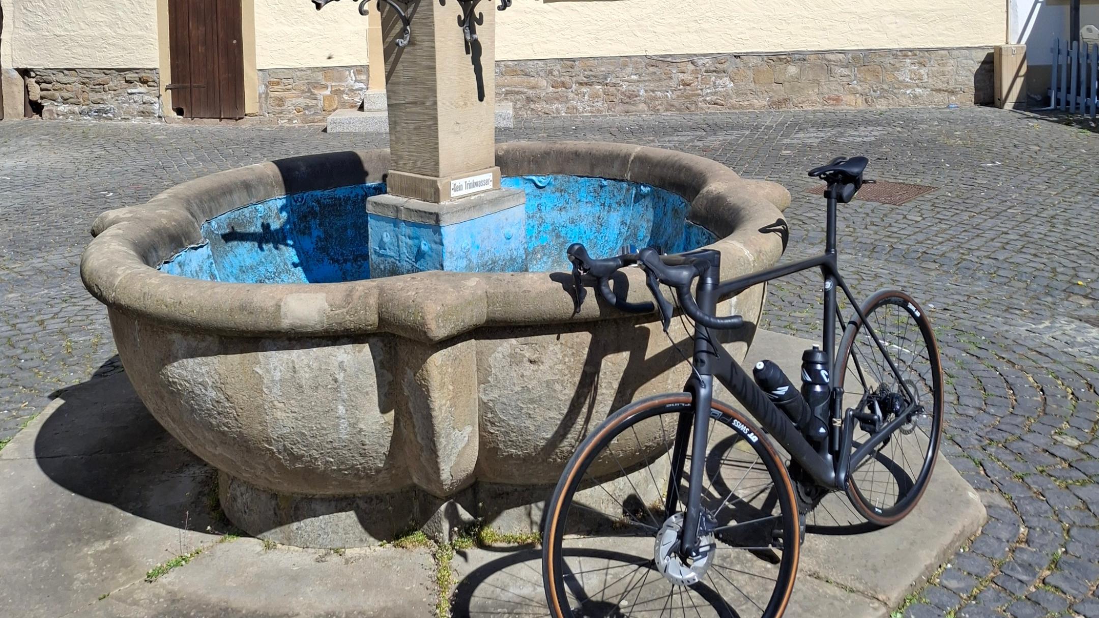 Ein Fahrrad lehnt an einem Brunnen vor einem Fachwerkhaus.