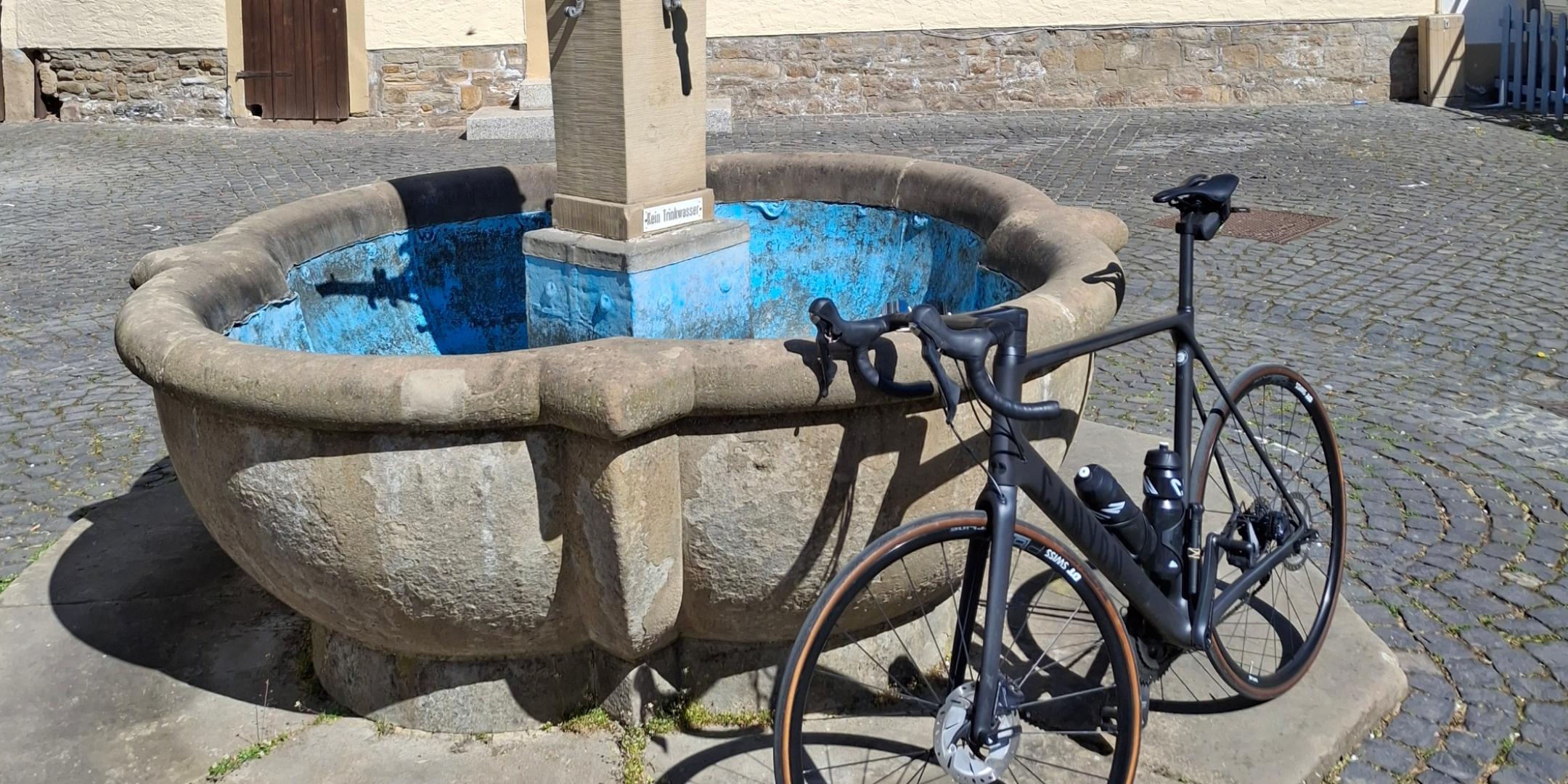 Ein Fahrrad lehnt an einem Brunnen vor einem Fachwerkhaus.