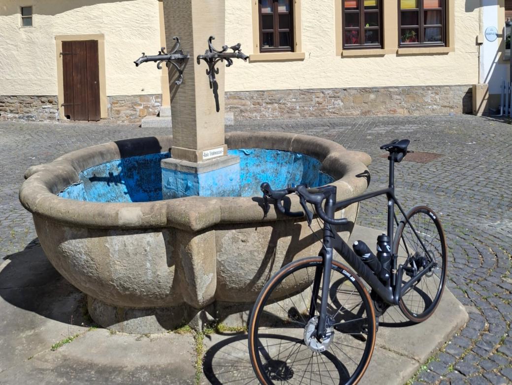 Ein Fahrrad lehnt an einem Brunnen vor einem Fachwerkhaus.