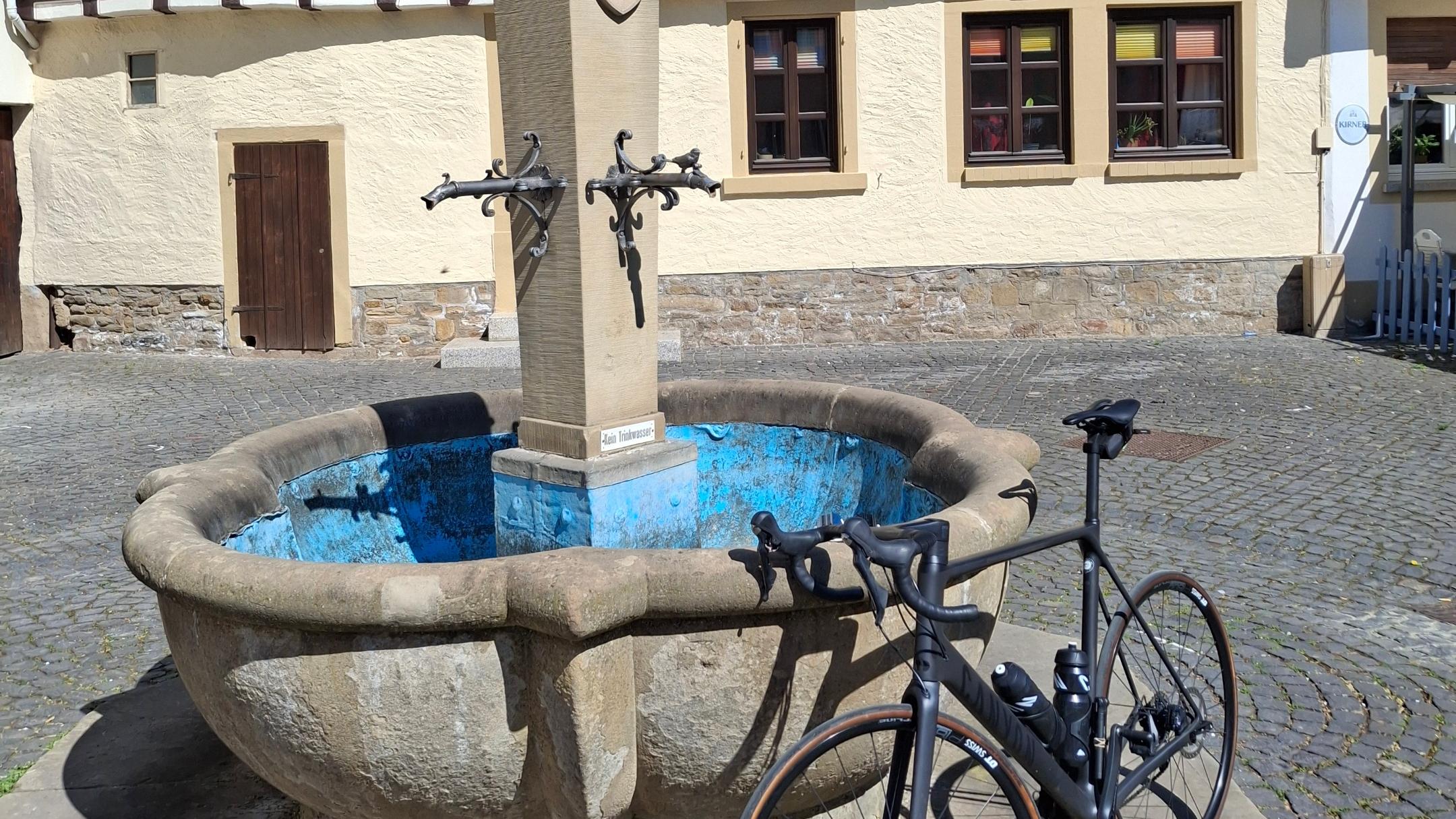 Ein Fahrrad lehnt an einem Brunnen vor einem Fachwerkhaus.