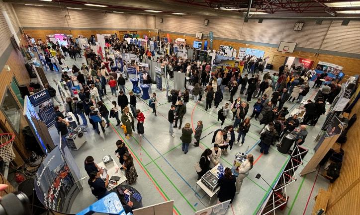 Blick über die mit Ausstellungsständen bestückte Turnhalle mit vielen Menschen