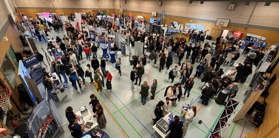 Blick über die mit Ausstellungsständen bestückte Turnhalle mit vielen Menschen