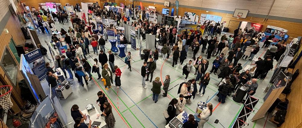 Blick über die mit Ausstellungsständen bestückte Turnhalle mit vielen Menschen