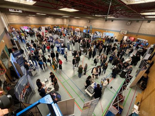 Blick über die mit Ausstellungsständen bestückte Turnhalle mit vielen Menschen