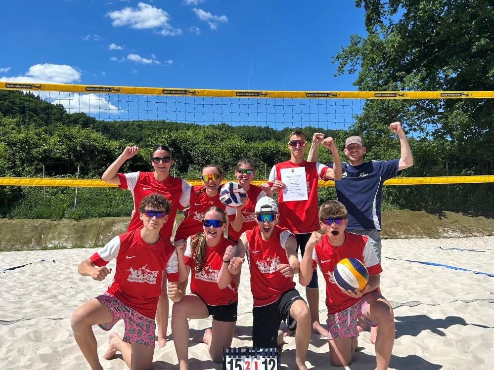 Junge Menschen posieren auf einem Beachvolleyballplatz.