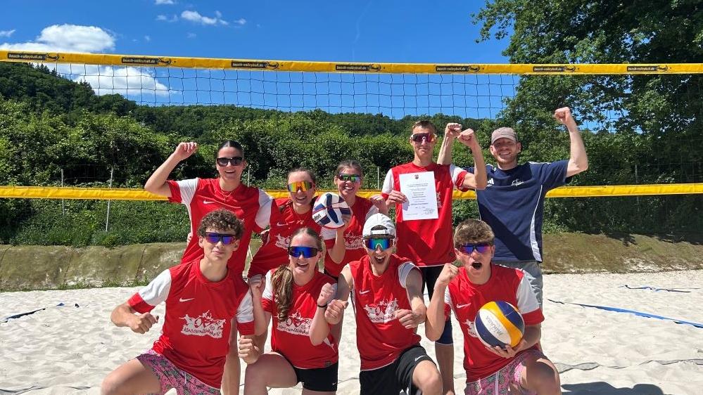 Junge Menschen posieren auf einem Beachvolleyballplatz.