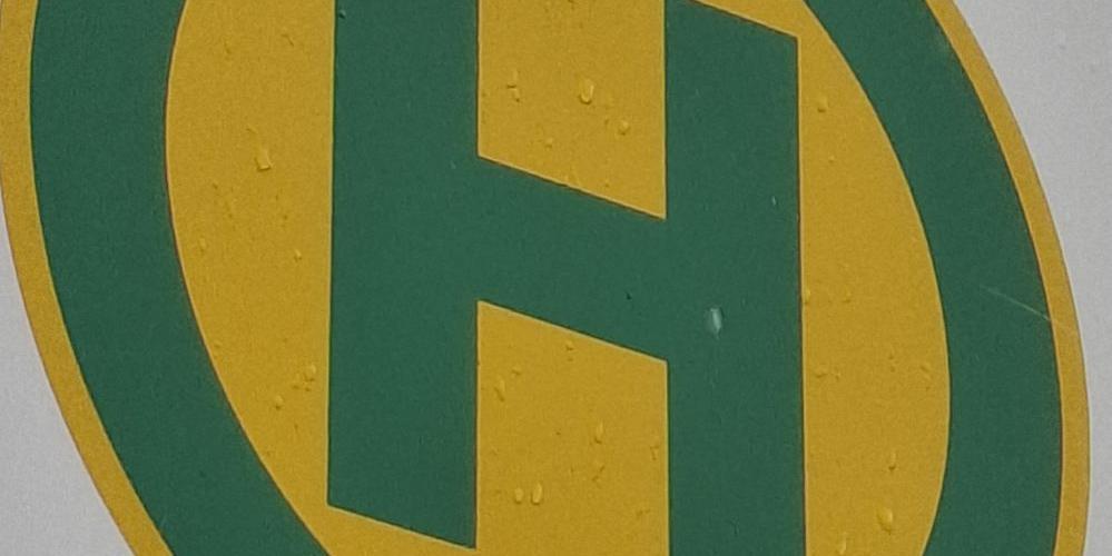 Bushaltestellensymbol: grüner Buchstabe H in grünem Kreis auf gelben Grund