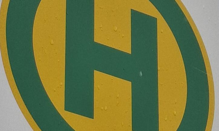 Bushaltestellensymbol: grüner Buchstabe H in grünem Kreis auf gelben Grund