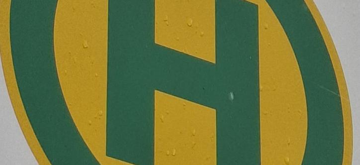 Bushaltestellensymbol: grüner Buchstabe H in grünem Kreis auf gelben Grund