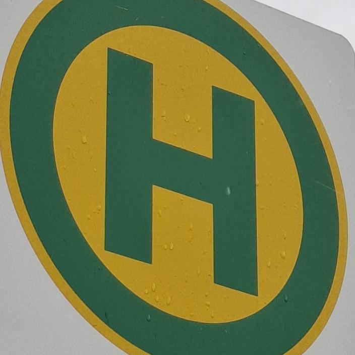 Bushaltestellensymbol: grüner Buchstabe H in grünem Kreis auf gelben Grund