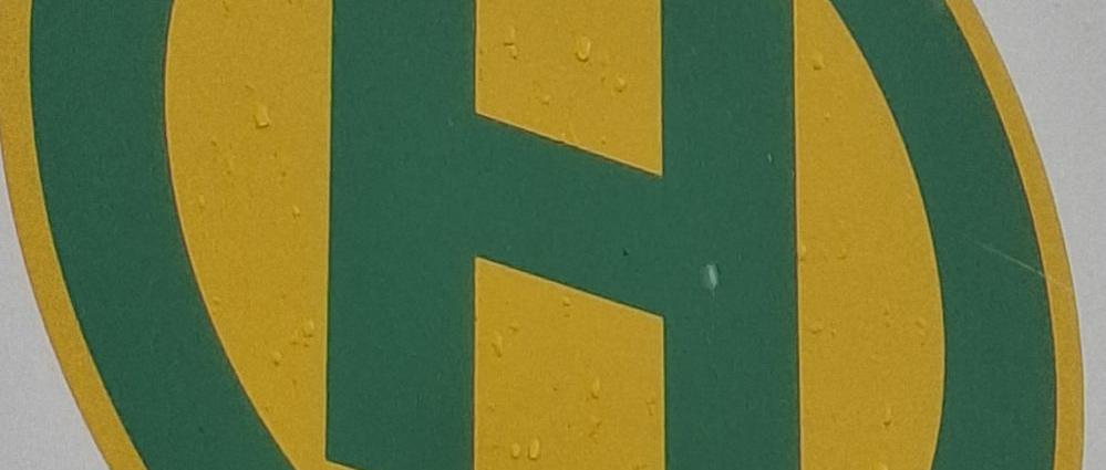 Bushaltestellensymbol: grüner Buchstabe H in grünem Kreis auf gelben Grund