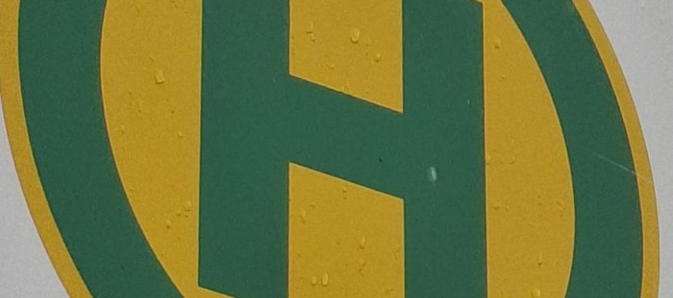 Bushaltestellensymbol: grüner Buchstabe H in grünem Kreis auf gelben Grund