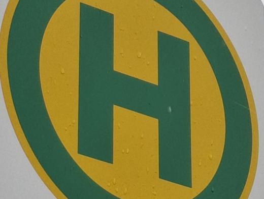Bushaltestellensymbol: grüner Buchstabe H in grünem Kreis auf gelben Grund