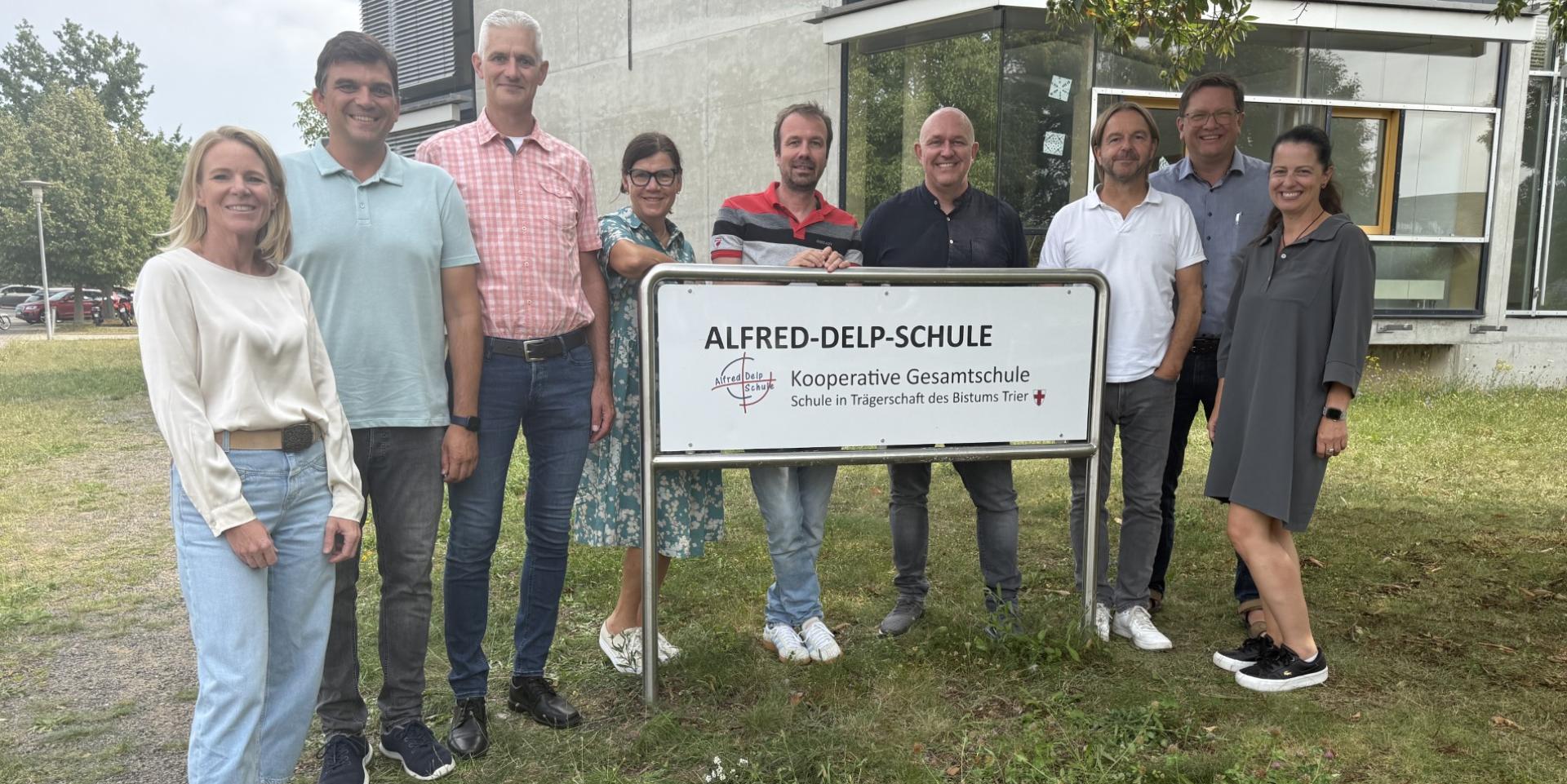 Die Schulleitung steht am Schulschild vor dem Neubau.